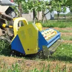 Trattore con falciatrice gialla e blu che lavora in un vigneto. L'erba tagliata copre il terreno, un segno di potenziale inquinamento del suolo se non gestita correttamente.