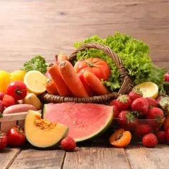 Un cesto traboccante di frutta di stagione giugno: fragole, melone, albicocche, anguria, carote, pomodori, lattuga e limone.