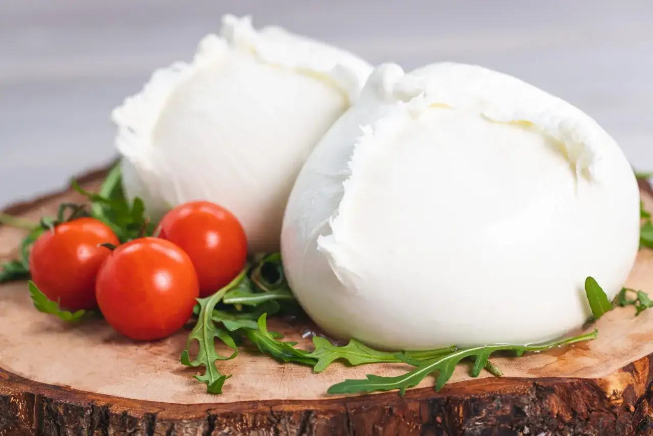 Due fresche mozzarelle di bufala salernitane, con pomodorini e rucola su un tagliere di legno.
